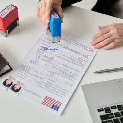 Pracownik stempluje dokument "Approved", związany z legalizacją pobytu cudzoziemców.