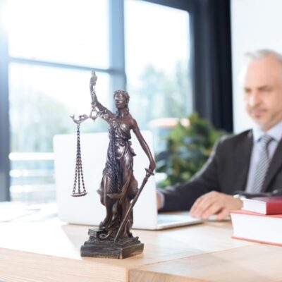 Adwokat w biurze z figurką sprawiedliwości na biurku.