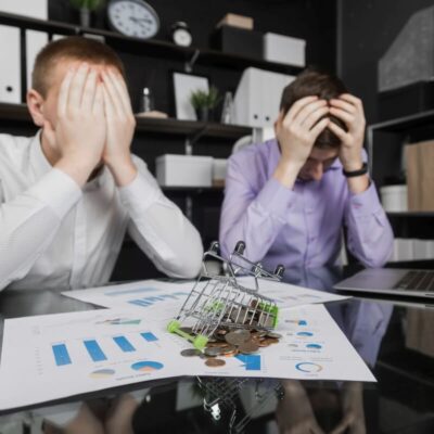 Dwóch zmartwionych mężczyzn w biurze analizuje dokumenty finansowe, zastanawiając się nad upadłością konsumencką.